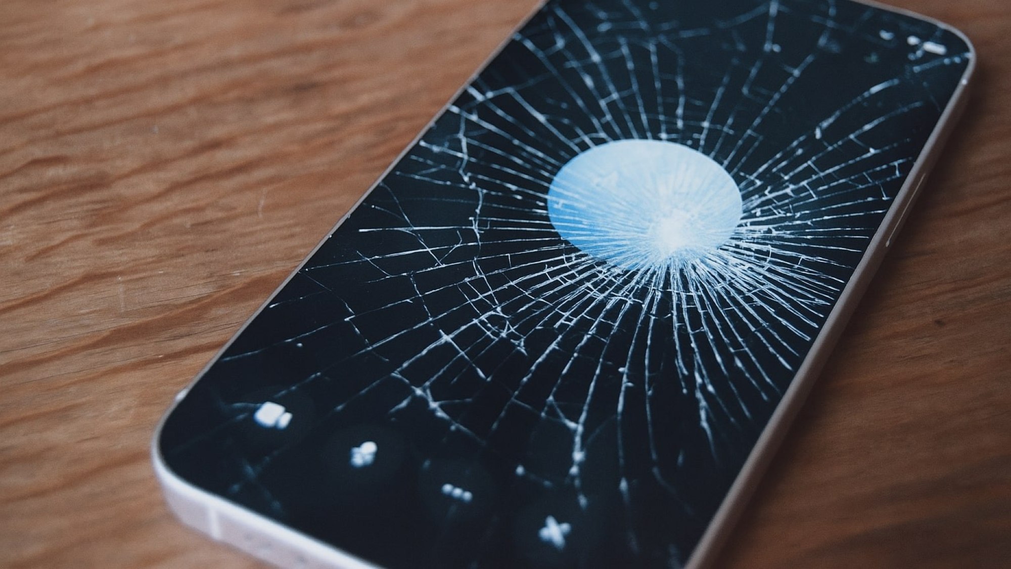 Ein Handy mit zersprungenden Display liegt auf einer Holztischplatte.