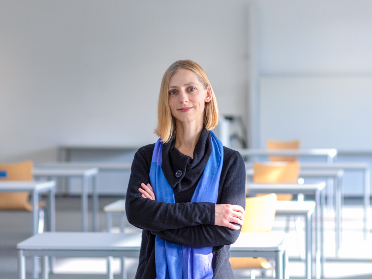 A person is standing in a seminar room and is looking into the camera.