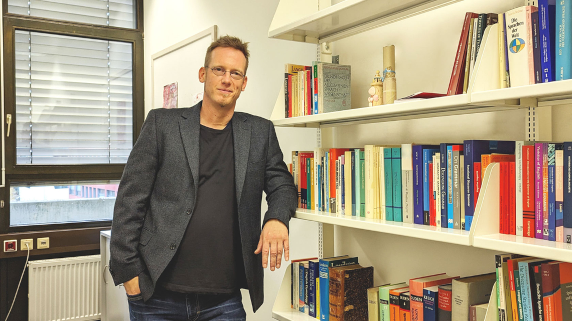 Andreas Jäger steht in seinem Büro neben seinem Bücherregal.